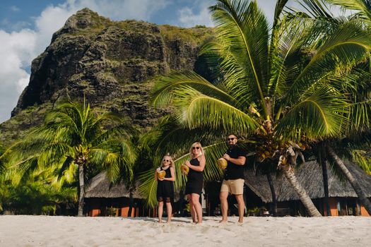 a stylish family in black clothes with coconuts in their hands on the beach of the island of Mauritius.Beautiful family on the island of Mauritius in the Indian ocean.