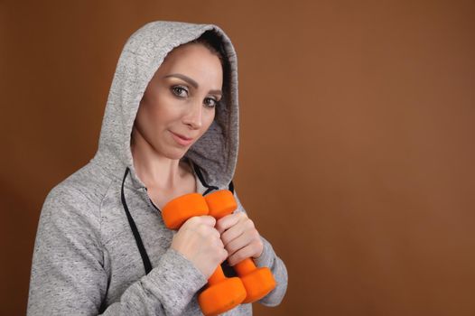 woman trainer in a hood with dumbbells in her hands. studio portrait.