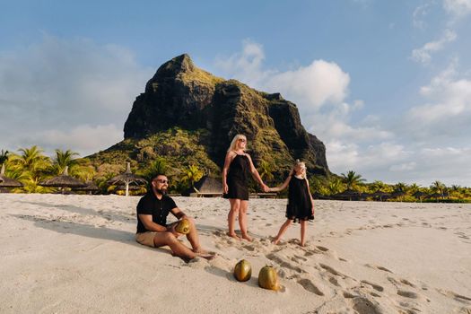 a stylish family in black clothes with coconuts in their hands on the beach of the island of Mauritius.Beautiful family on the island of Mauritius in the Indian ocean.