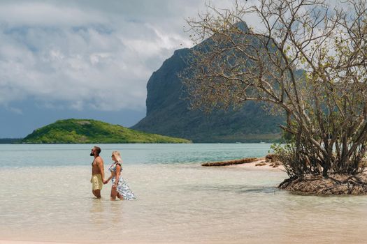 A girl in a swimsuit and a man in shorts stand in the ocean against the backdrop of mount Le Morne on the island of Mauritius.A couple in the water look into the distance of the ocean against the background of mount Le Morne .