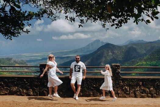 a happy family, a man, a woman and a daughter, are jumping merrily against the background of mountains and jungles of the island of Mauritius.A couple and daughter in the jungle of the island of Mauritius in white clothes walking in Africa