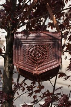 small burgundy women's leather bag with a carved pattern. street photo