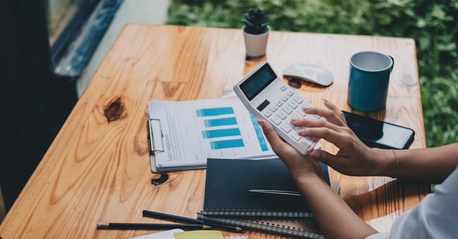 Woman entrepreneur using a calculator in her hand, calculating financial expense at home office