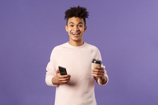 Waist-up portrait of happy enthusiastic hispanic man with smartphone, hold mobile phone and drinking coffee from take-away cup in office cafe, discuss recent project coworkers and team.