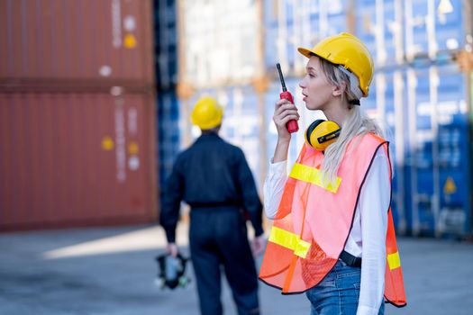 Foreman or cargo container woman worker use walkie talkie to communicate with her team and co-worker technician stand on background.