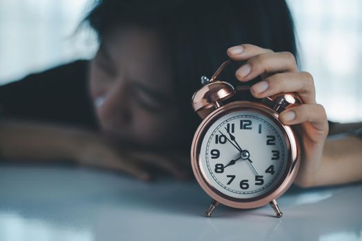 The lazy asian woman lay down on the table and reached out to turn off the alarm clock for lifestyle concept