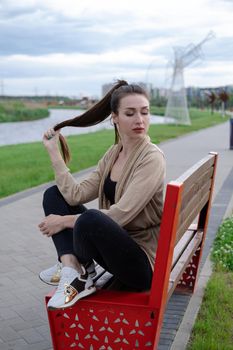 attractive brunette woman sitting on a bench in park. fashion clothes, stylish look.