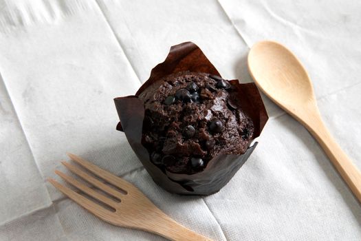 Chocolate muffin in brown paper cup with dark chocolate  topping and wooden spoon and fork 
