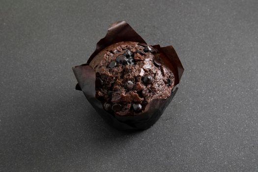 Chocolate muffin in brown paper cup with chocolate pieces on black background