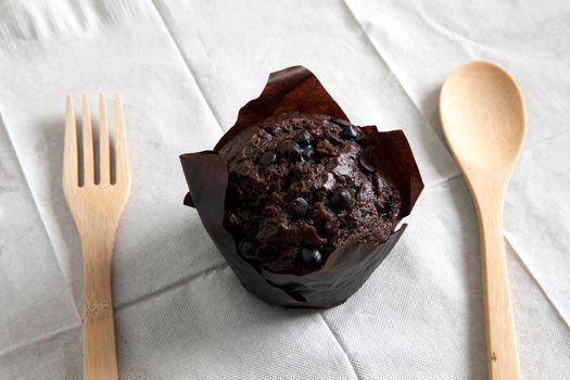 Chocolate muffin in brown paper cup with dark chocolate  topping and wooden spoon and fork 