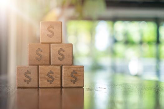 A set of wooden cubes on a table with a dollar symbol on the background as a metaphor for money or wealth saving and financial freedom.