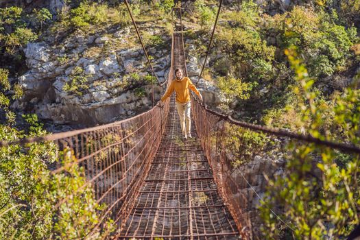 Man tourist on Old rusty bridge. Attraction Long extreme suspension iron bridge across the river Moraca. Sights of Montenegro. Landmark Montenegro.