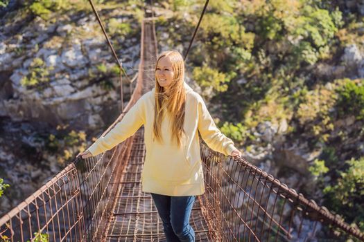 Woman tourist on Old rusty bridge. Attraction Long extreme suspension iron bridge across the river Moraca. Sights of Montenegro. Landmark Montenegro.