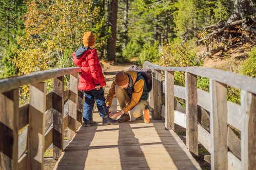 Dad tying his son's shoelaces on a wooden bridge.