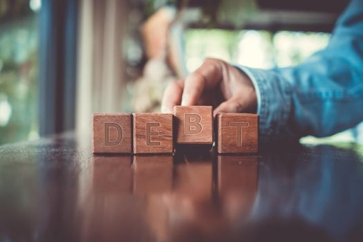 A group wooden cubes on table with word Debt on it background.