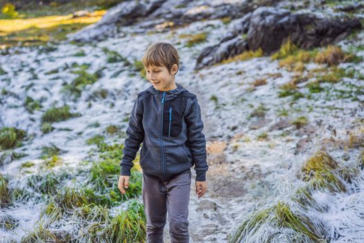 The boy is surprised at the first snow that fell on the green grass.