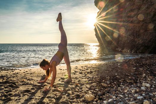 Girl gymnast is training on the beach by the sea sunset. Does twine. Photo series