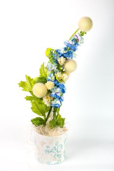 Composition with artificial flowers in a pot on white background. Ekibana from white and blue artificial flowers and green leaves.