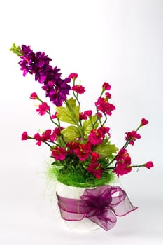 Composition with artificial flowers in a pot on white background. Ekibana from red and blue artificial carnations and green leaves.