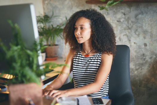 Shot of an attractive young african woman sitting alone and using her computer to work from home stock photo