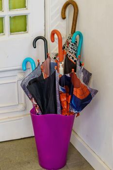 Umbrellas of various colors inside a container at the door of a house. Concept of rain and bad weather