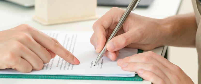 Businesswoman signs agreement contract with another businesswoman at the office. Close up shot at the woman's hand. Concept of business partnership and legal activities of lawyer.