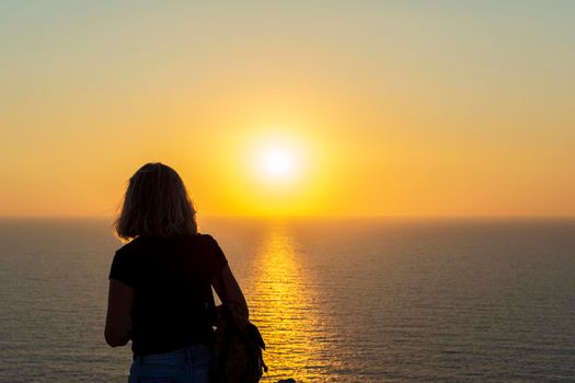 Silhouette of a woman at orange sunset on a cliff overlooking the sea at Palaiokastro castle of ancient Pylos. Greece.