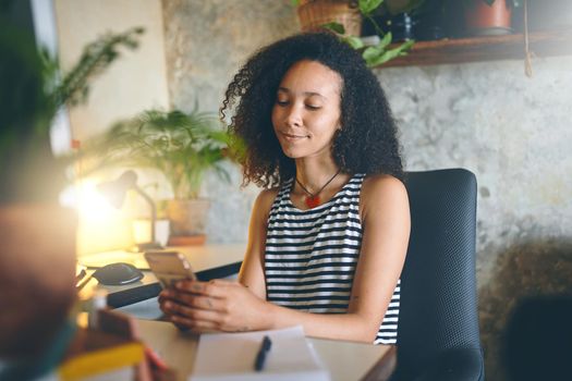 Shot of an attractive young woman sitting alone and using her cellphone to work from home stock photo