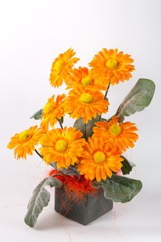 Composition with artificial flowers in a pot on white background. Ekibana from orange artificial gerberas.