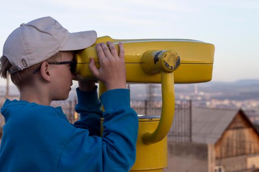 Boy looking through binocular at the city on the pointview