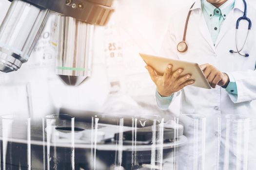 Medical science research and development concept - Doctor holding tablet computer with scientific instrument, microscope and chemical test tube in lab background.