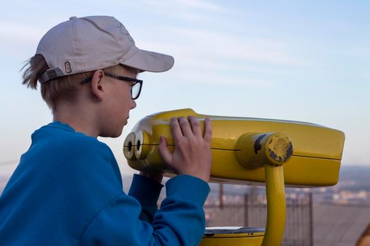 Boy looking through binocular at the city on the pointview