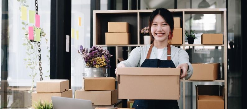 Small business owner concept, Portrait young attractive asian female owner startup business work happy with box at home prepare parcel delivery in sme supply chain..