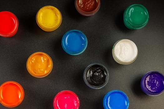 full-frame close-up background of opened small gouache paint jars on flat black surface