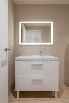 Modern bathroom with beige tiles, furniture and rectangular large mirror with lighting.