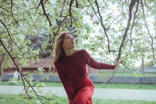 a girl in red admiring the cherry blossoms in the garden. sunny spring day