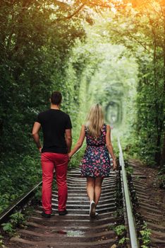 Loving couple in a tunnel of green trees on railroad.