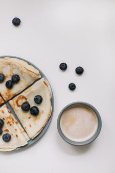 breakfast with a cup of cappuccino and pancakes with berries on a white background top view.