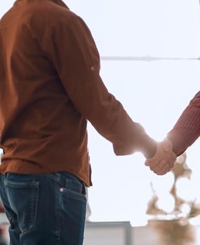 closeup of handshake between two men in the background of the office.