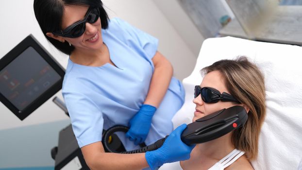 Beautician removing unwanted facial hair of client using laser in beauty salon. Aesthetic medicine laser hair removal concept