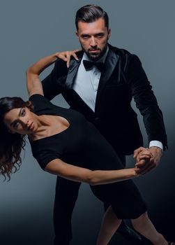 Well-dressed retro couple dancing tango over grey studio background