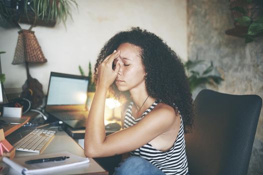 Shot of an attractive young african woman sitting alone and feeling stressed while using her computer to work from home stock photo