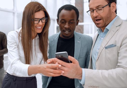 smiling colleagues looking at the smartphone screen, standing in a modern office
