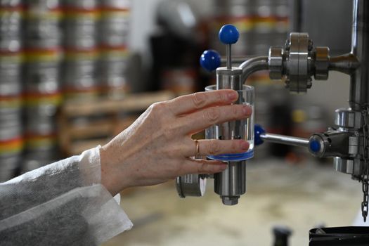 Hand turns the tap on the background of beer production