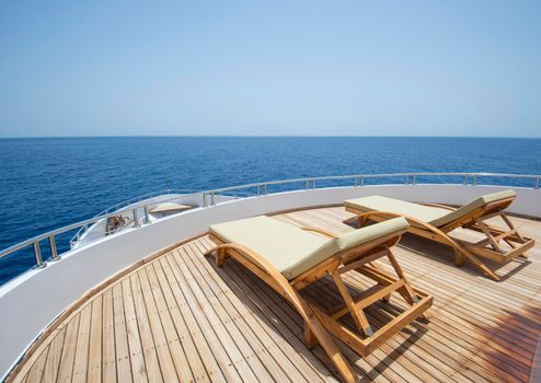 Teak bow sundeck of a large luxury motor yacht out at sea with sunbeds and a tropical ocean view background