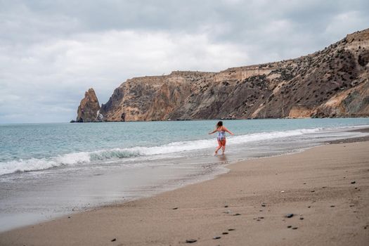 A plump woman in a bathing suit enters the water during the surf. Alone on the beach, Gray sky in the clouds, swimming in winter