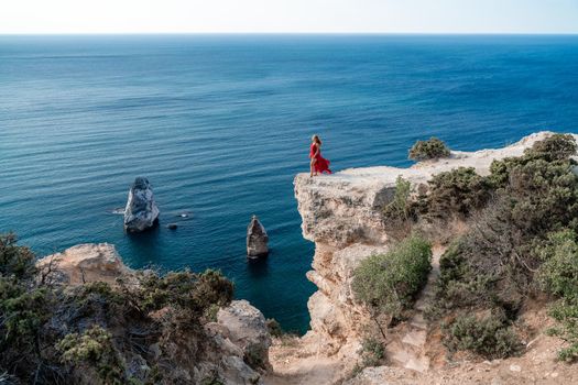 A woman in a red flying dress fluttering in the wind, against the backdrop of the sea