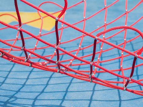 Red net on blue background. Sport equipment on public sportsground in sunny day. Geometrical shadows in sunny day.