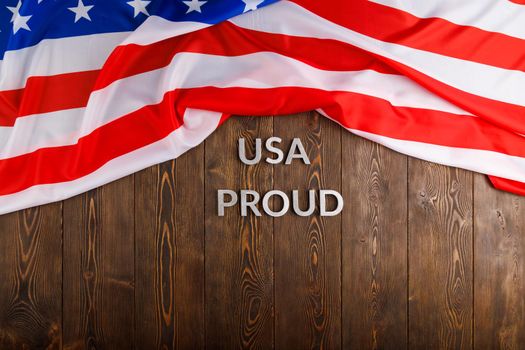 words USA proud laid with silver metal letters on brown wooden surface with flag of United States of America. High angle view.