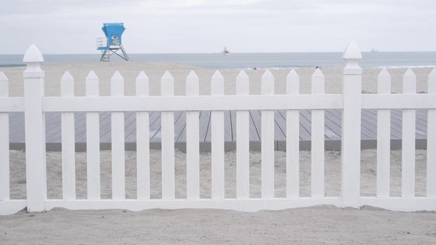 Lifeguard stand or life guard tower hut, surfing safety on California beach, USA. Rescue station, coast lifesavers wachtower or house, Coronado ocean beach, San Diego shore. White wooden picket fence.